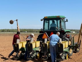 Men loading seed onto a tractor in field, wide shot